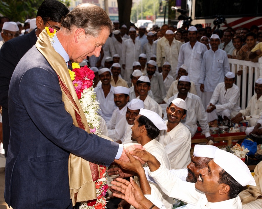 A garlanded visitor in a suit greeting seated dabbawalas