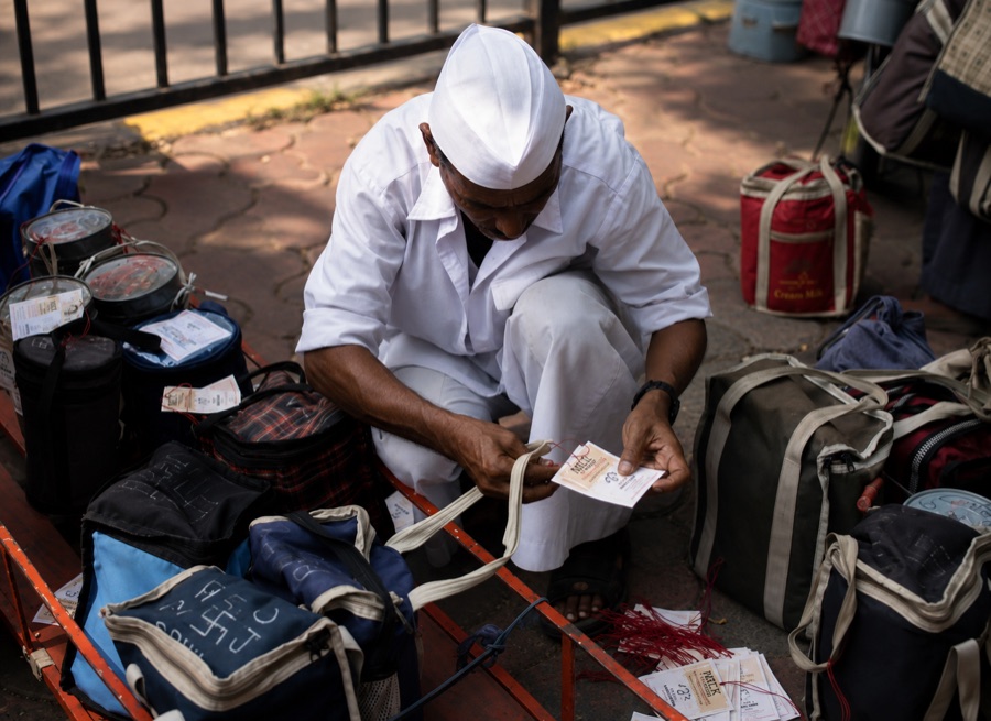 A dabbawala crouched over packed bags, sorting delivery slips