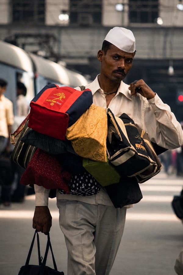A dabbawala walking with several loaded bags slung over his shoulder